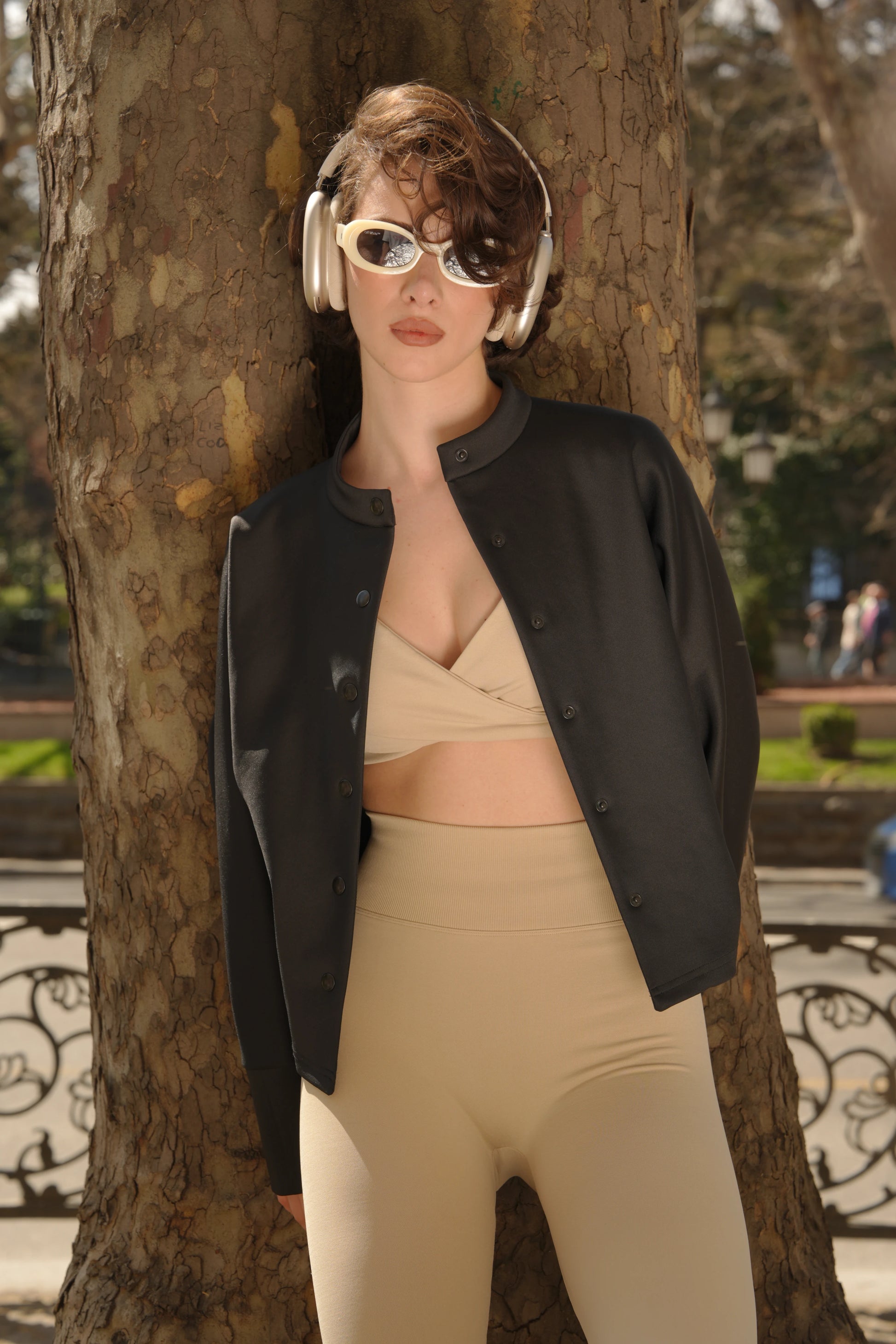 Person wearing a black blazer and beige pants standing next to a tree in an outdoor setting %Cream% %Hover%