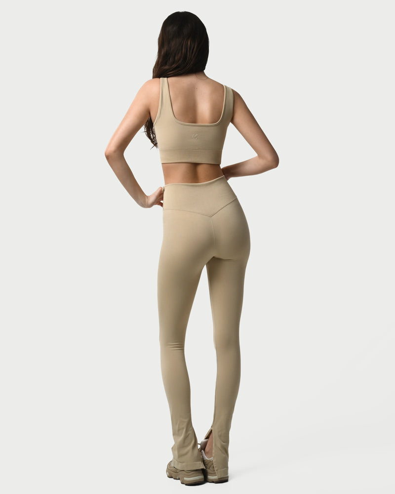 Woman wearing a beige sports bra and leggings on a white background