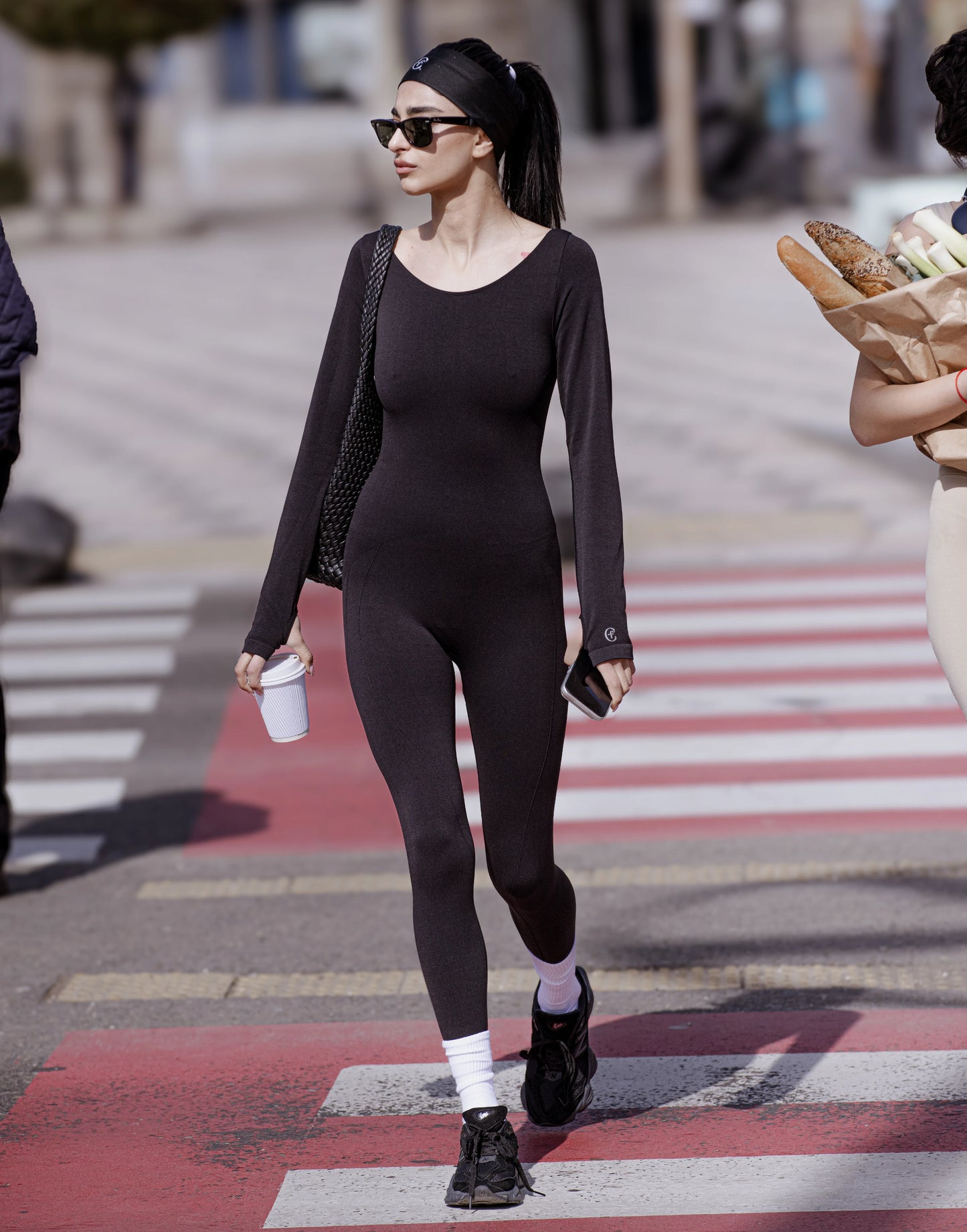Person in a black outfit crossing a street with a crosswalk. %Black% %Hover%